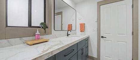 A bathroom with a marble countertop, a mirror, a sink, a towel rack, and a door.
