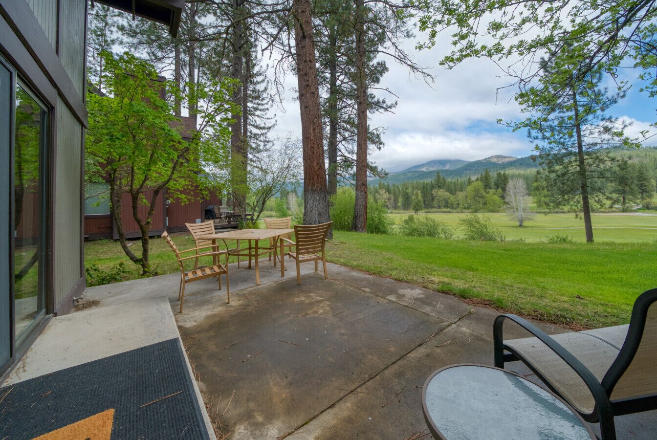A patio with a table and chairs, surrounded by trees and a view of a green landscape.
