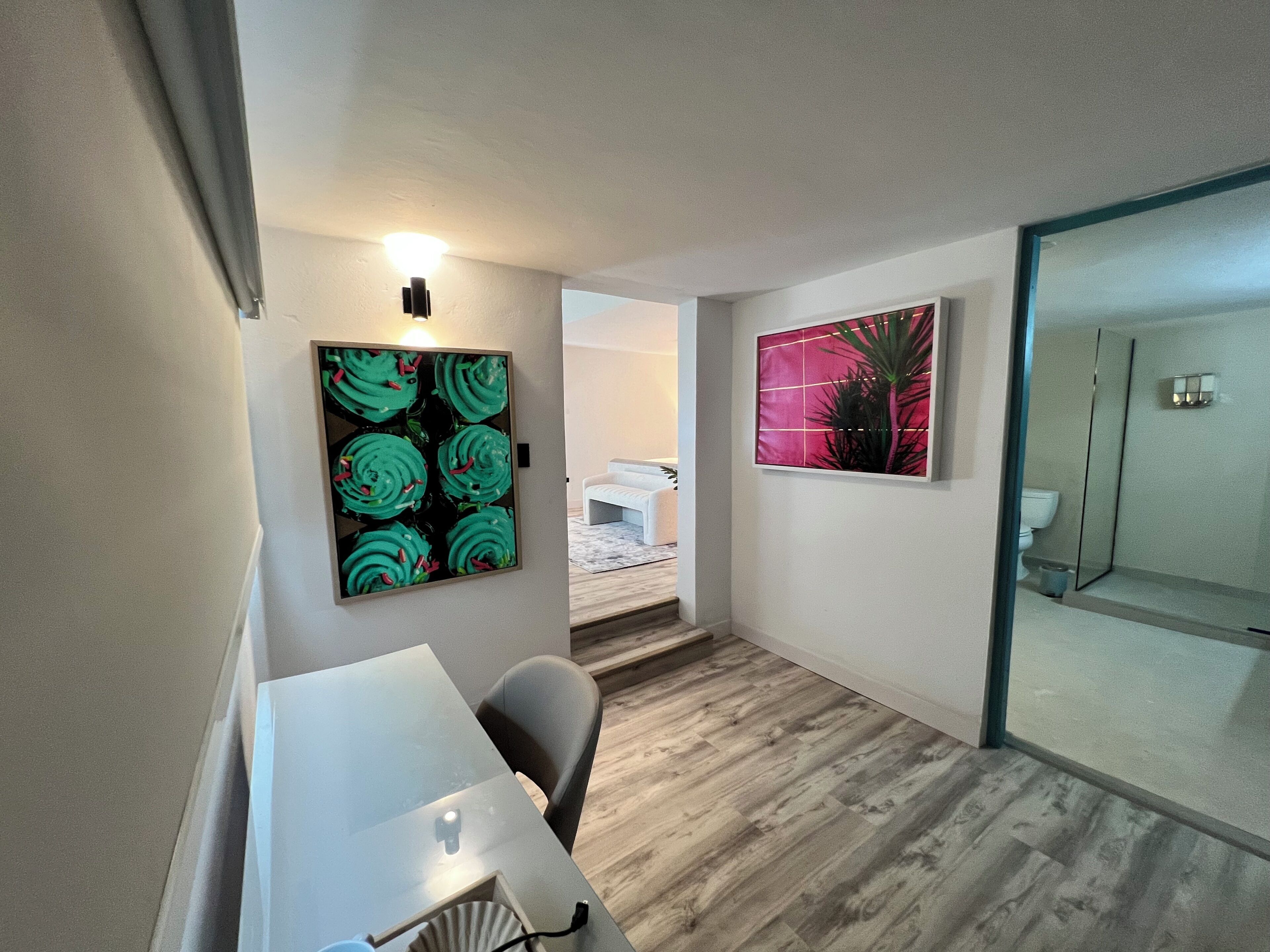Una habitación moderna con una mesa de comedor, dos sillas, una lámpara de pared y dos obras de arte enmarcadas.