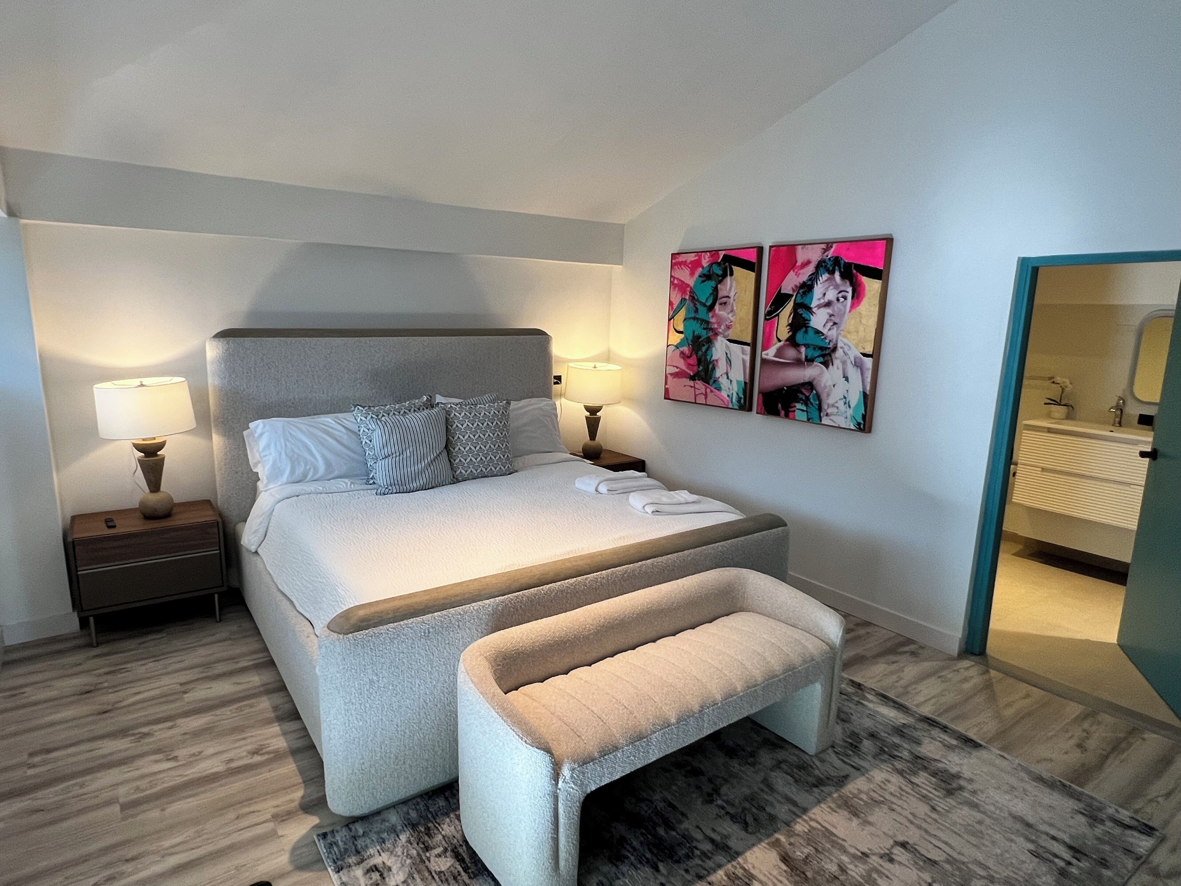 Una camera da letto moderna con un letto grande, abat-jour, una panca e due opere d'arte appese al muro.