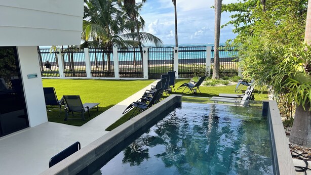 A swimming pool with lounge chairs, a grassy lawn, and a view of the ocean. - Villa Paradiso (San Juan)