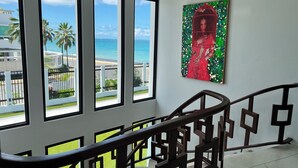 A staircase with a railing, large windows with a view of the beach and ocean, and a painting on the wall. - Villa Paradiso (San Juan)