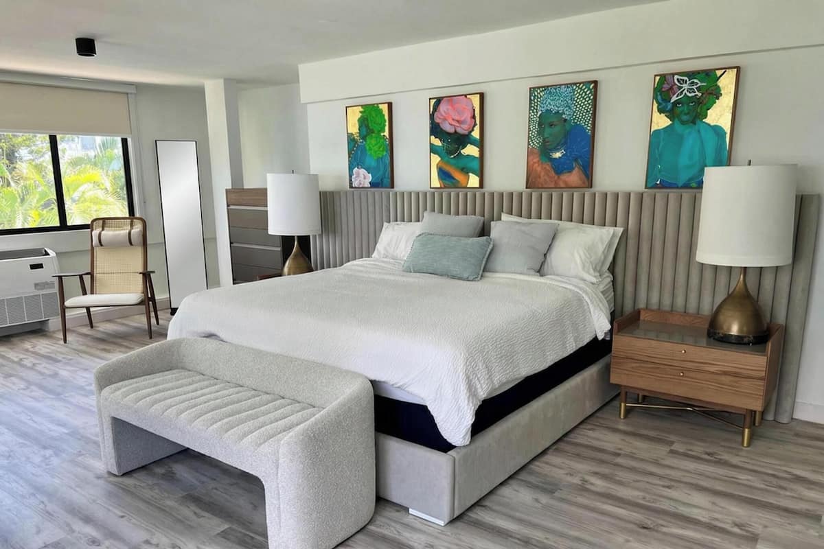 A modern bedroom with a large bed, bedside tables, a bench, and artwork on the wall.