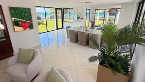 A spacious living area with a large window, a dining table, and a comfortable seating arrangement. - Villa Paradiso (San Juan)