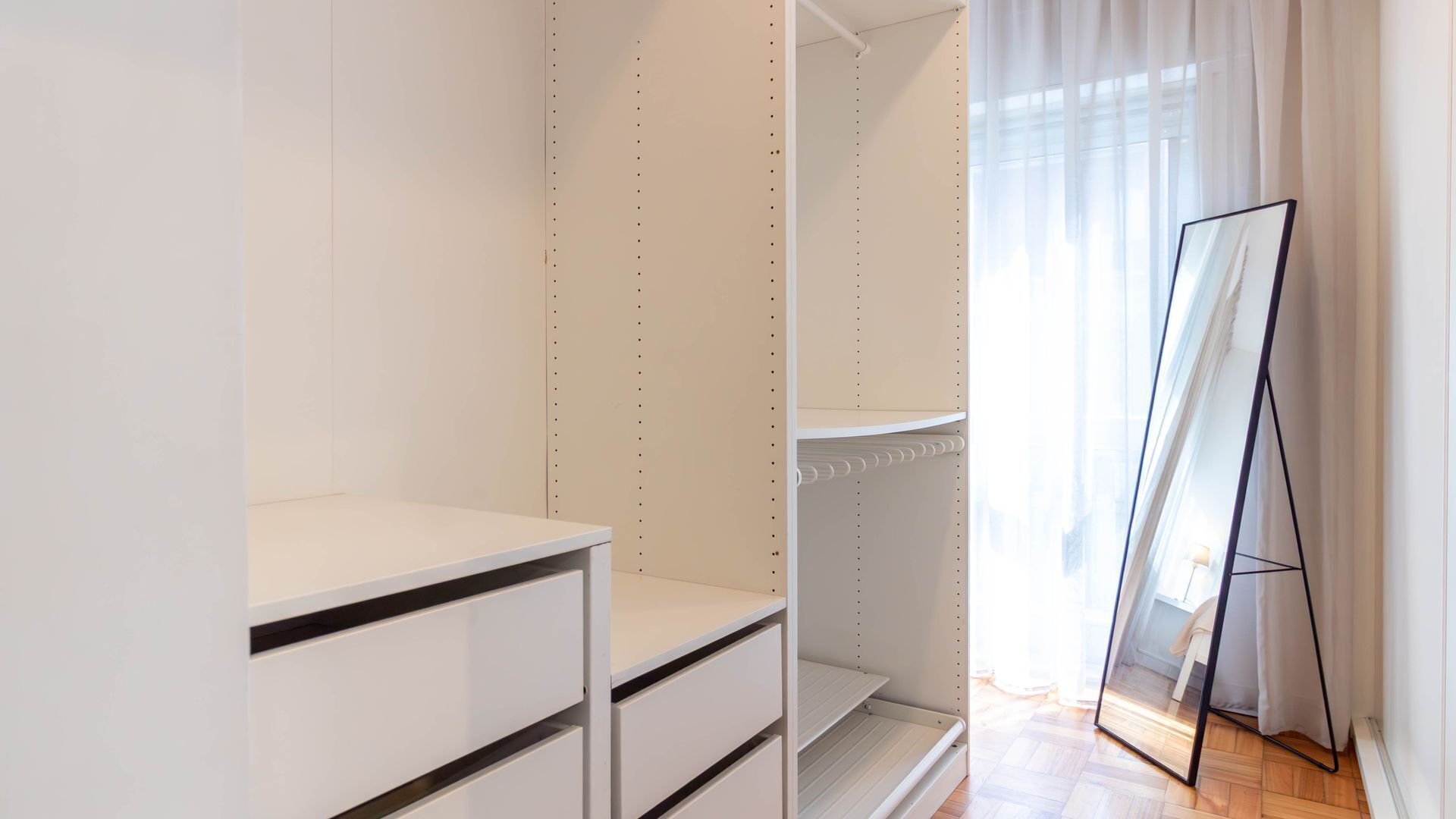 A walk-in closet with open shelving, a mirror, and a view of a balcony with a curtain.