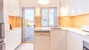 A modern kitchen with white cabinets, a dishwasher, a sink, and a window with a view of buildings. - Stylish 3BR in Central Porto w/ AC by LovelyStay (Porto)