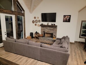 Ein modernes Wohnzimmer mit einer Eckcouch, einem Kamin aus Stein, einem Flachbildfernseher und dekorativer Wandkunst.