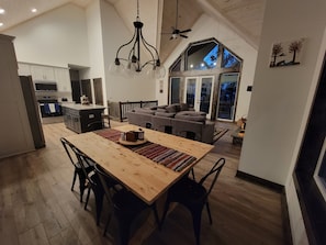 Eine geräumige Küche mit modernen Geräten, eine Essecke mit Holztisch und -stühlen sowie ein gemütlicher Wohnbereich mit großem Fenster mit Blick ins Freie.