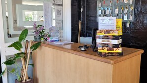 A hotel reception desk with a wooden counter, a potted plant, a menu board, and a wall-mounted key rack. - El Mirador (Villa Carlos Paz)