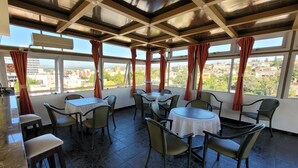 A restaurant with multiple tables and chairs, large windows with curtains, and a view of the cityscape. - El Mirador (Villa Carlos Paz)