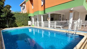 A swimming pool with a wooden deck, surrounded by a building with balconies and air conditioning units. - El Mirador (Villa Carlos Paz)