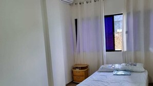 Un dormitorio con dos camas, una ventana con cortinas, una mesita de noche de madera y un aire acondicionado.