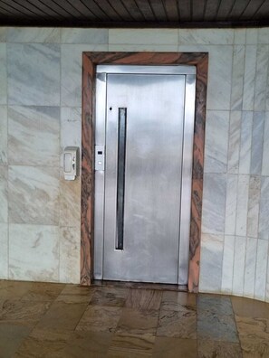 A metallic elevator door with a vertical handle, set in a tiled wall with a marble-like pattern. - Barra Lighthouse. SPACIOUS. Feet in the sand. SEA VIEW. (Salvador)