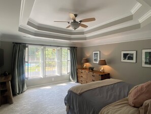 Une chambre à coucher avec un lit, une commode, un ventilateur de plafond et une fenêtre avec des rideaux.