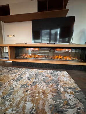 A modern living room with a fireplace, a flat-screen TV mounted above it, and a patterned rug on the floor. - Luminar Aurelia suite,
Luxury Penthouse (London)
