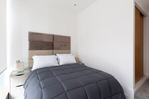 A modern bedroom with a large bed, a bedside table, and a wooden wardrobe. - Luminar Aurelia suite (London)