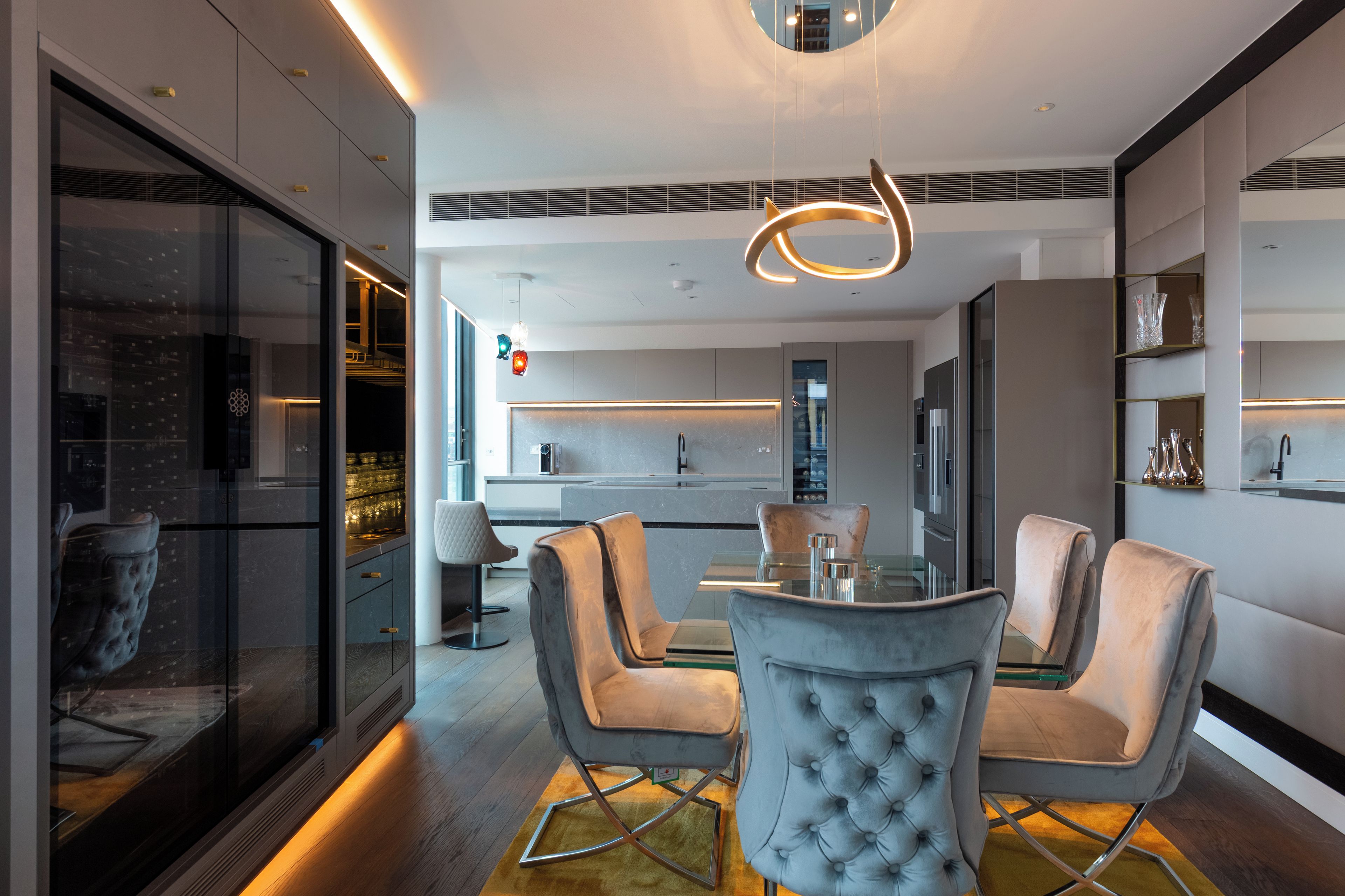 Un intérieur moderne avec un coin repas agrémenté de fauteuils capitonnés et d’une table en verre, une cuisine dotée d’un îlot central et une vue dégagée grâce à un mur en verre.