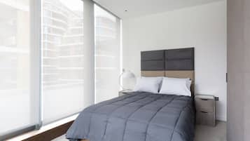 Una camera da letto moderna con un'ampia finestra, un letto con copriletto grigio, due comodini e una lampada a parete.
