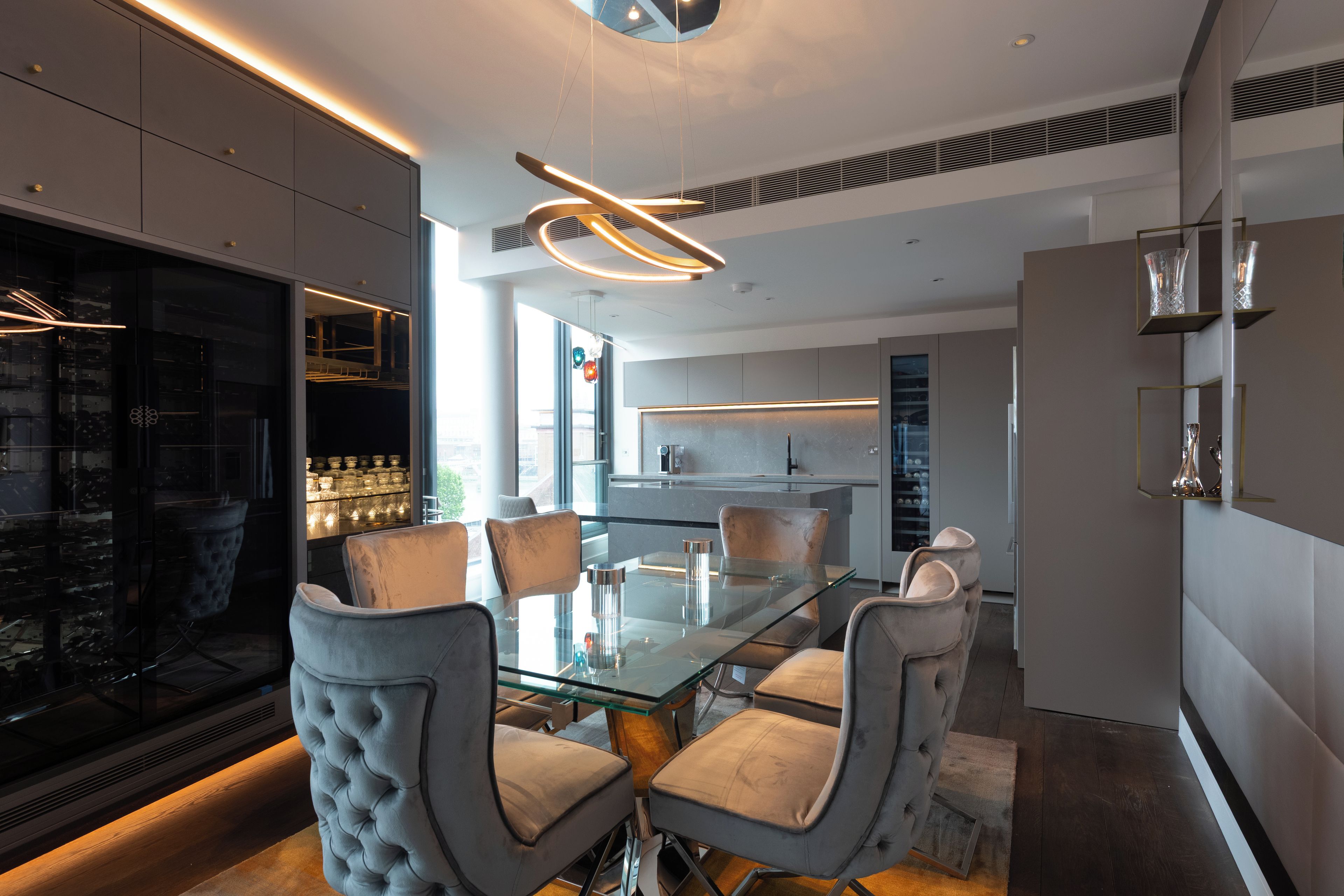 Una cucina moderna con un tavolo da pranzo in vetro, sedie rivestite di grigio ed elettrodomestici integrati.