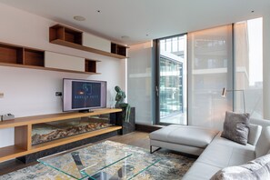 A modern living room with a flat-screen TV, a glass coffee table, a sofa, and a fireplace with a stone surround. - Luminar Aurelia suite (London)