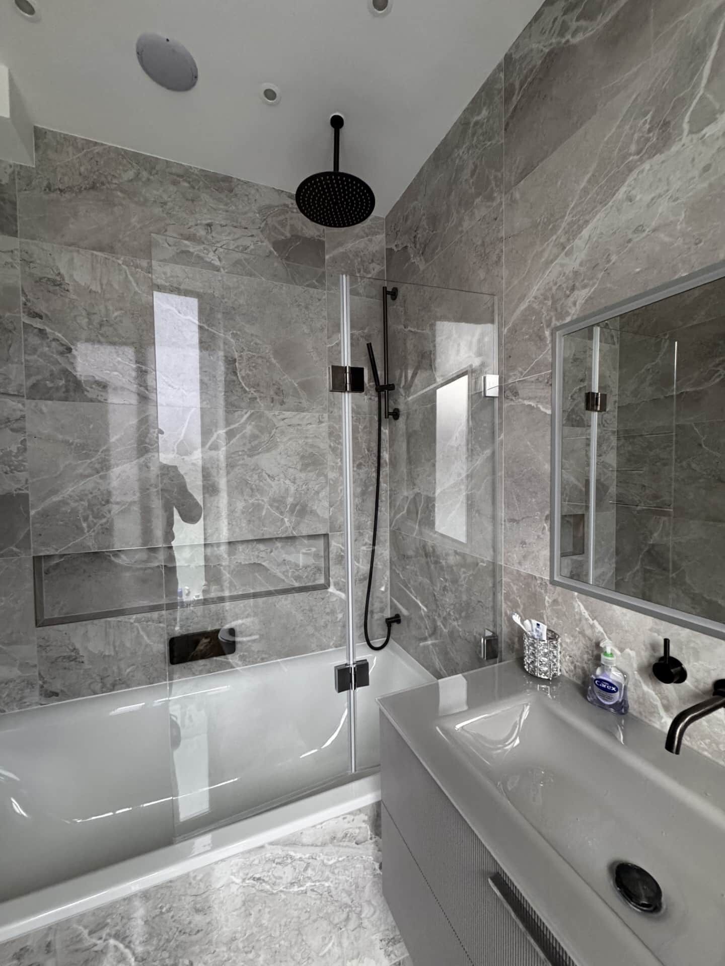 A modern bathroom with a glass-enclosed shower, a large mirror, and a vanity with a sink.