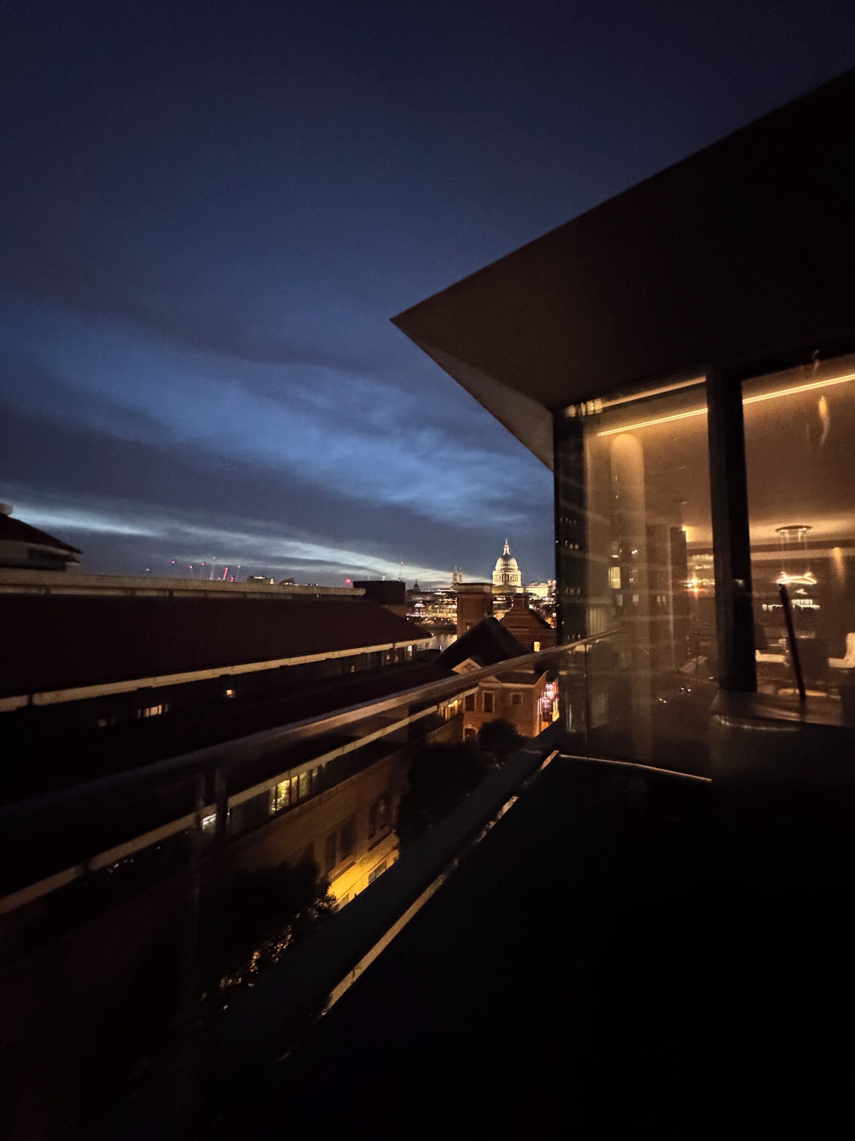 Un edificio moderno con una grande facciata vetrata, vista sullo skyline cittadino e una struttura a cupola ben visibile in lontananza.