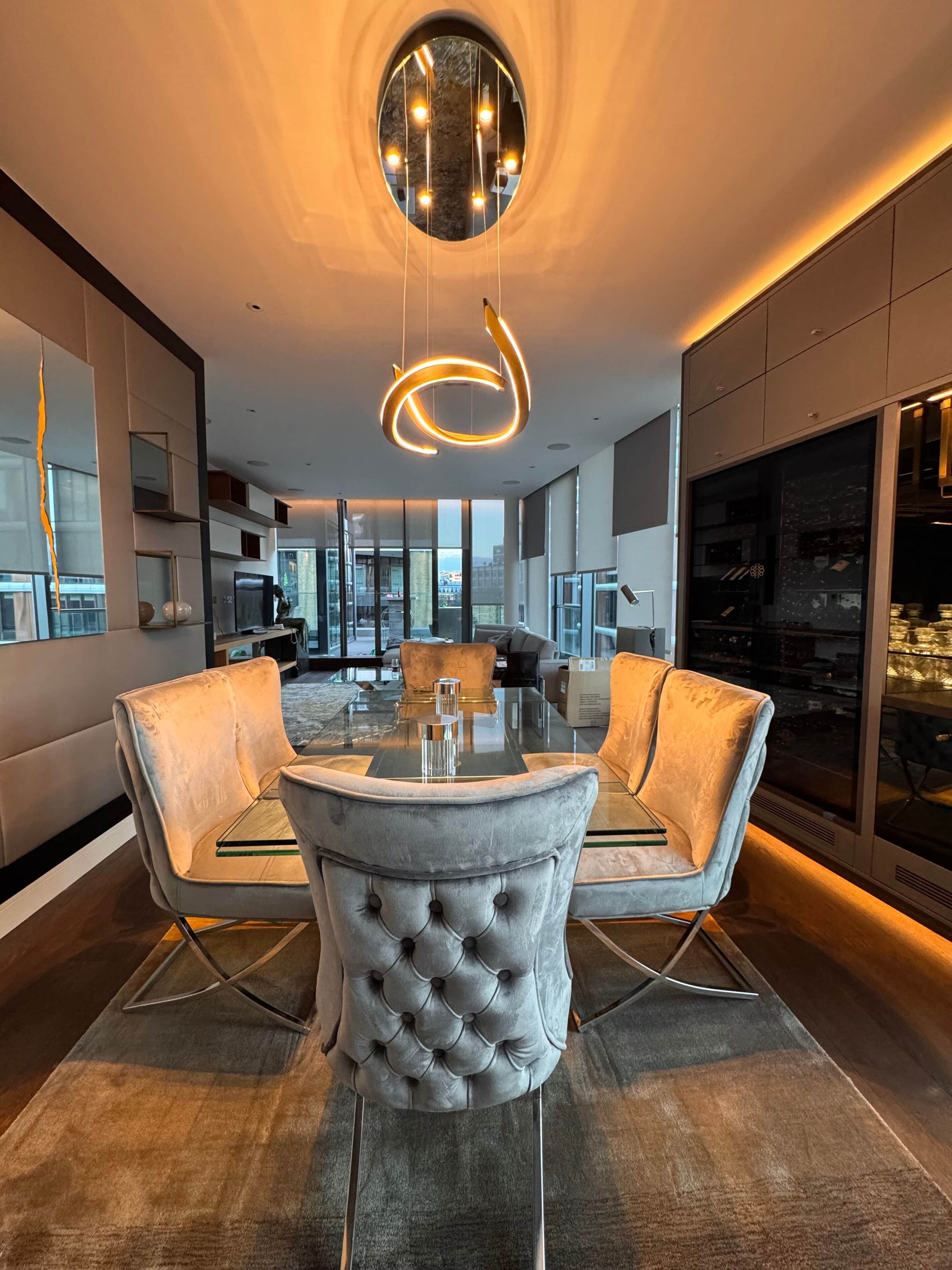 A modern dining area with a glass table, tufted chairs, and a unique circular light fixture.