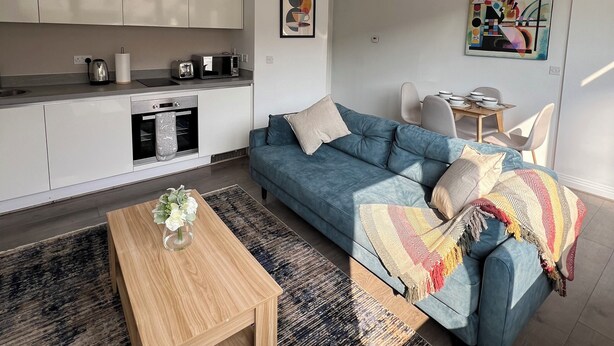 Un salon moderne comprenant un canapé, une table basse et un coin cuisine avec des placards et des appareils électroménagers.