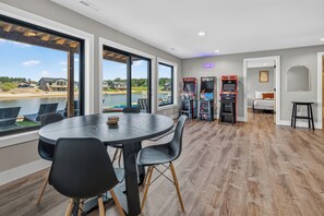 A dining area with a large table and chairs, arcade games, and a view of a lake. - NEW*Lakefront-Private Chef-Beach + Kayaks-WI Dells (New Lisbon)