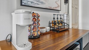 Máquina de café com porta-cápsulas e cafeteira sobre bancada de madeira.