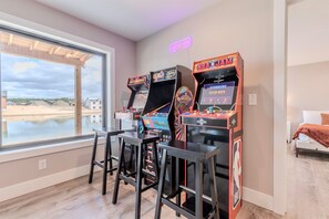 A room with arcade games, a window with a view of a construction site, and a bed with a brown blanket.