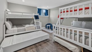 Quarto infantil com beliches, uma janela com cortinas e uma cadeira azul pequena.