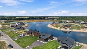 Zona residencial com casas perto de um lago, com céu claro e uma ponte ao longe.