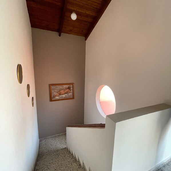 A staircase with a round window, a framed artwork, and a ceiling light.