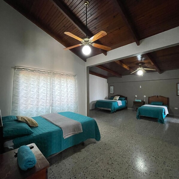 A room with three beds, a ceiling fan, and a window with curtains.