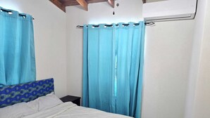 Una camera da letto con un letto, un comodino, una finestra con tende e una ventola a soffitto.