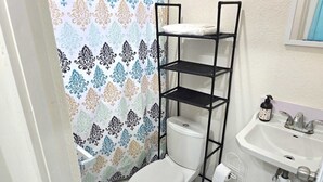 Un bagno con il water, uno scaffale, un lavandino e una tenda da doccia.