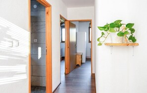 Ein Flur mit einer Holztür, einer Pflanze auf einem Regal und einem Blick in einen Küchenbereich.