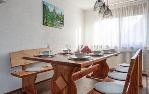 Ein Essbereich mit einem Holztisch, der für sechs Personen gedeckt ist, einer Bank und einem Fenster mit Vorhängen.