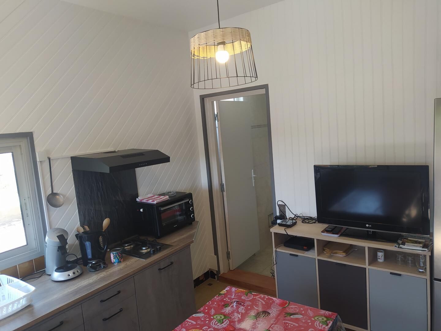 A compact kitchen with a microwave, toaster, and coffee maker, a television on a stand, and a door leading to a bathroom.