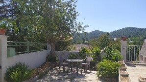 Eine Terrasse mit Tisch und Stühlen, umgeben von Grünpflanzen und Blick auf Hügel.