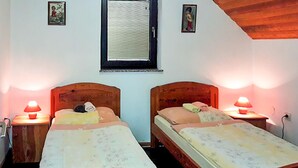 Två separata sängar med trägavlar, sänglampor, ett fönster med persienner och två små tavlor som hänger på väggen.