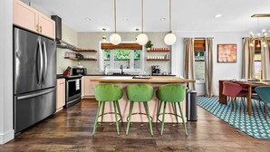 Eine moderne Küche mit einem Edelstahl-Kühlschrank, einer Holzinsel mit Barhocker, Pendelleuchten und einem Essbereich mit einem gemusterten Teppich.