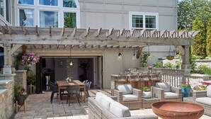 Un patio al aire libre con mobiliario de mimbre, un hogar para fogata y macetas colgantes.