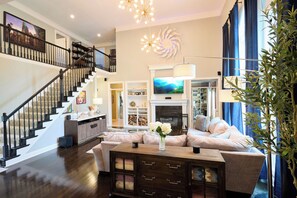 Un salón amplio con chimenea, un televisor grande y una escalera que sube a un nivel superior.