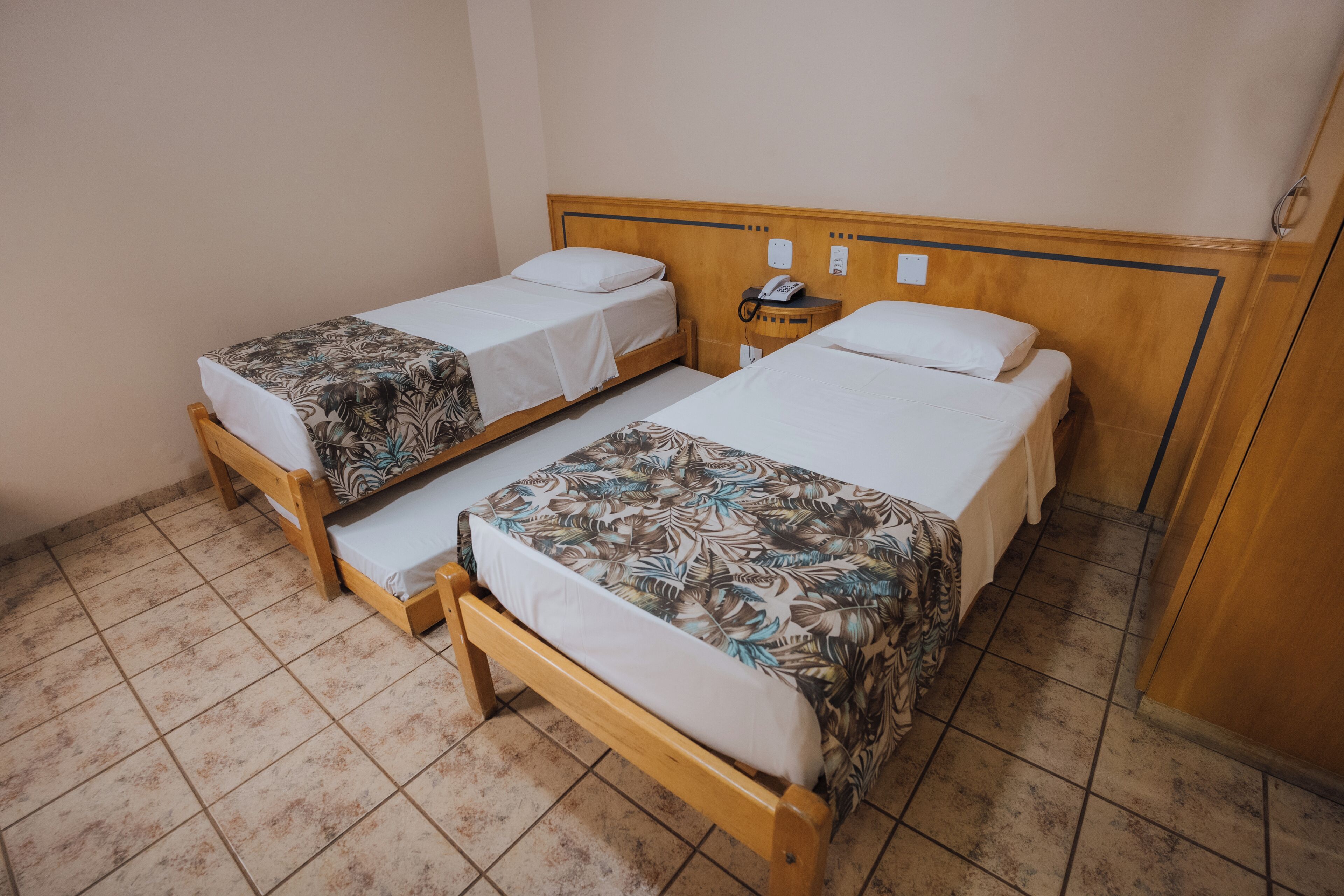 A room with two single beds, a wooden headboard, a bedside table with a phone, and a wall socket.