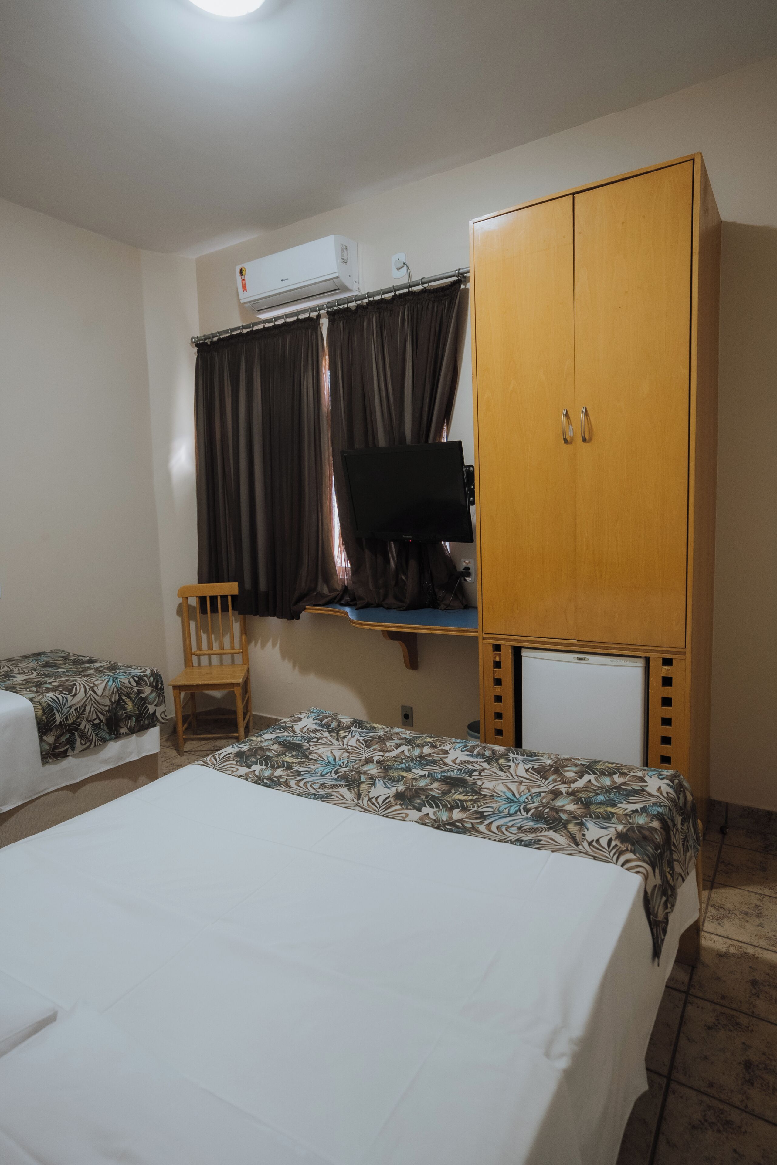 Un dormitorio con dos camas, un armario de madera, una televisión y un equipo de aire acondicionado.