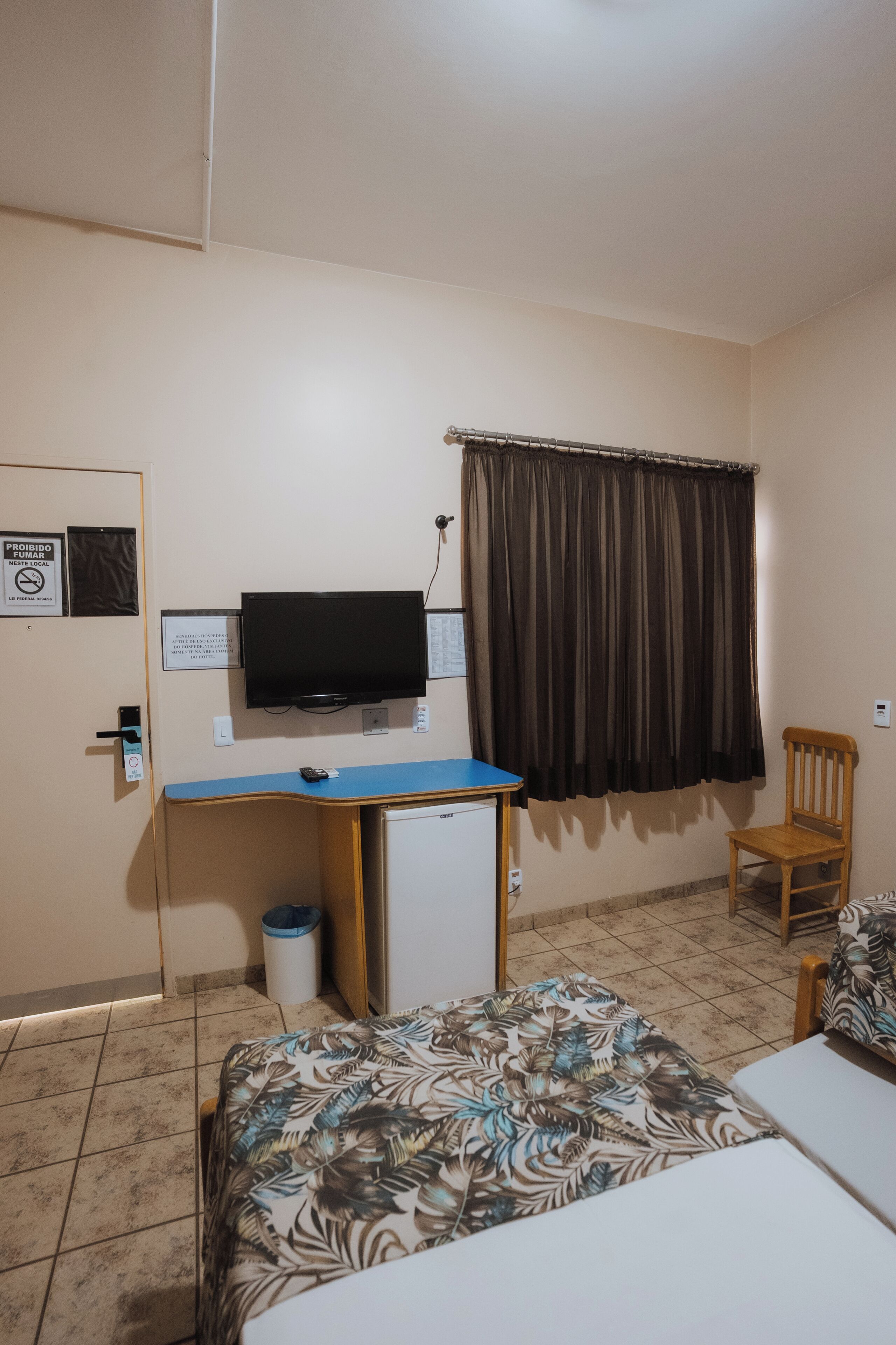A hotel room with a bed, a desk with a television, a chair, and a curtain.