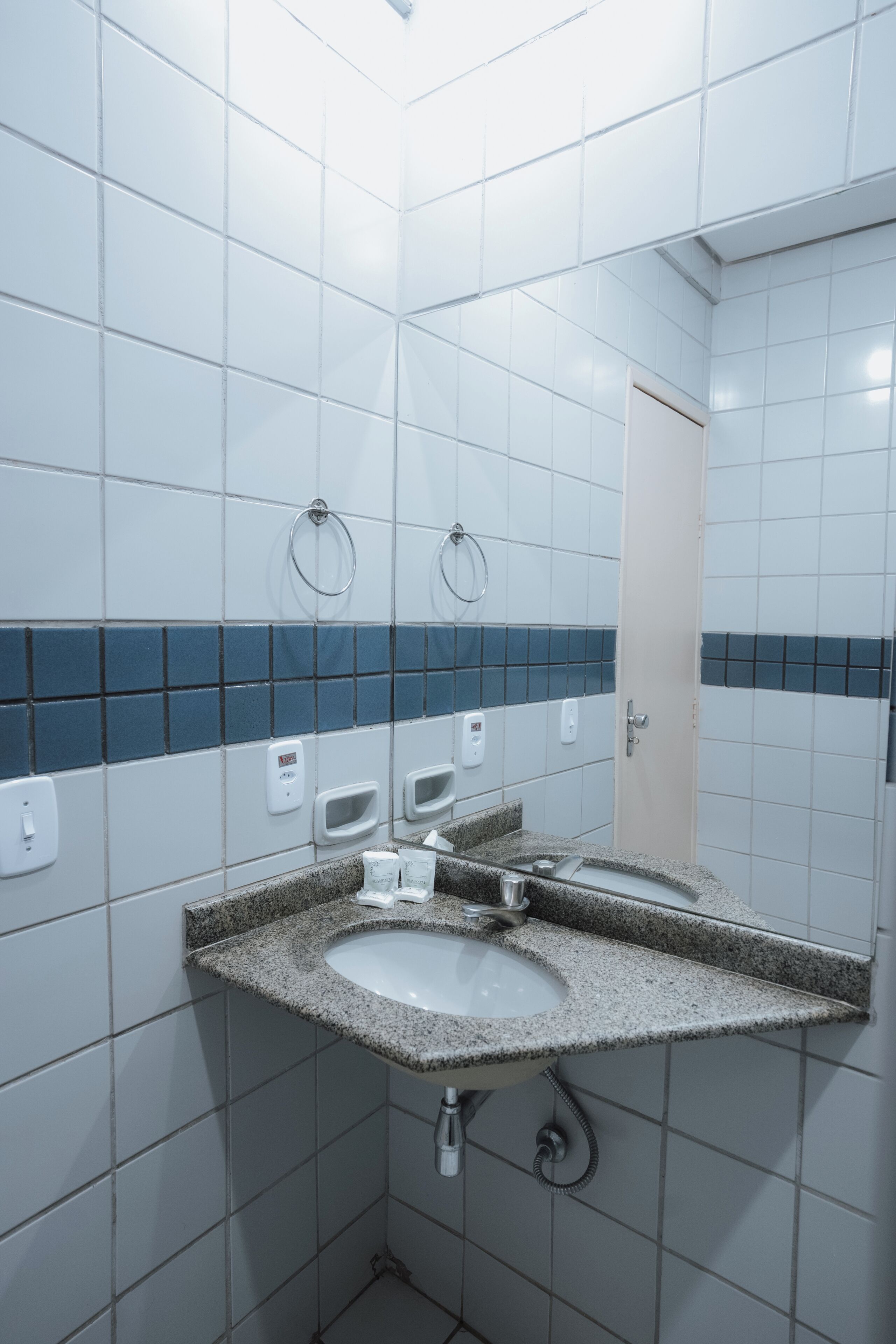 Une salle de bain avec des carreaux blancs, un comptoir en granit, un lavabo, un miroir et un porte-serviettes.