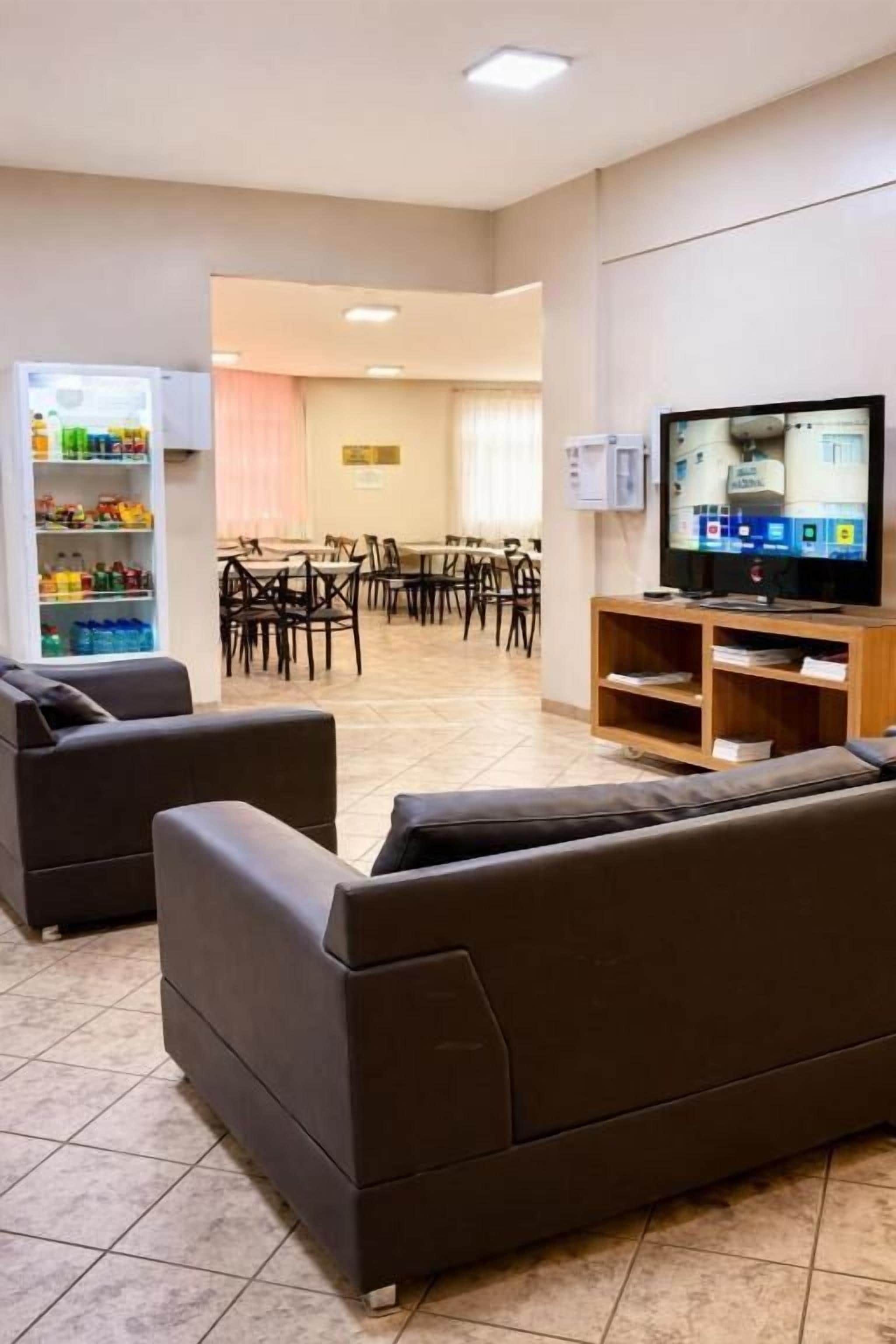 Un espacio de sala de estar con televisor, sofás, un refrigerador para bocadillos y un comedor con sillas y mesas.